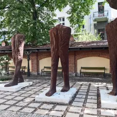 Trzy monumentalne rzeźby nóg, jakby wyrzeźbione majzlem z pnia drzewa, stoją na placu.