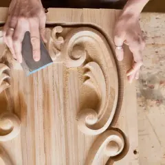 Ręce rzeźbiarza szlifują ozdobny ornament z litego drewna orzech.