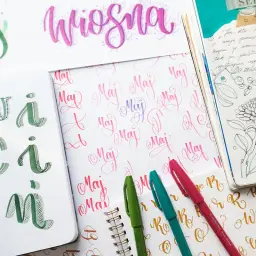 Artystyczny styl pisania. Na zdjęciu widać litery "maj" i "wiosna" wykonane różnymi technikami kaligrafii.