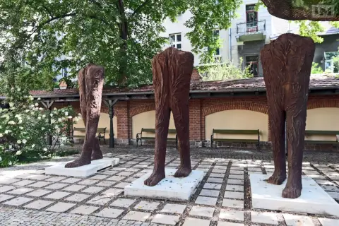 Trzy monumentalne rzeźby nóg, jakby wyrzeźbione majzlem z pnia drzewa, stoją na placu.