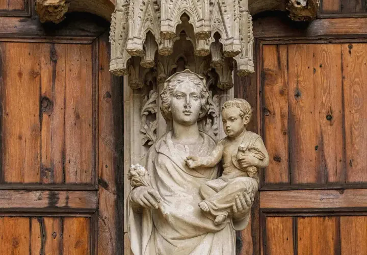 Kamienna rzeźba Matki Boskiej z Dzieciątkiem na tle drewnianych drzwi, symbolizująca teocentryzm i boską obecność w codzienności.