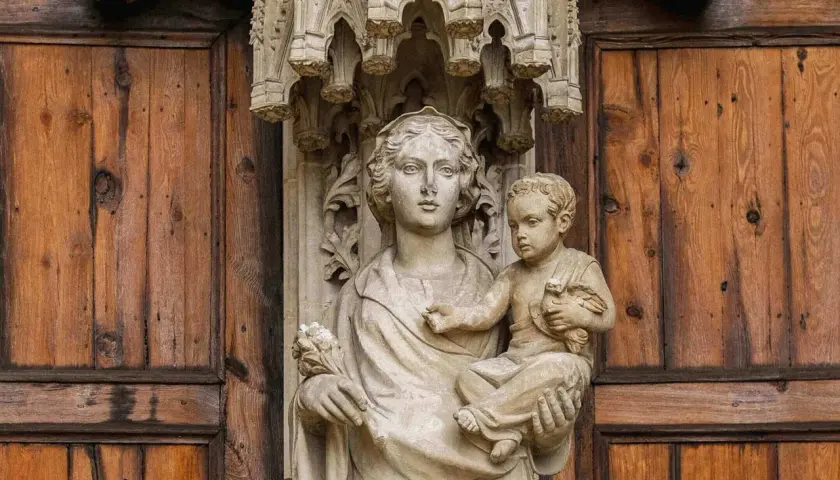 Kamienna rzeźba Matki Boskiej z Dzieciątkiem na tle drewnianych drzwi, symbolizująca teocentryzm i boską obecność w codzienności.