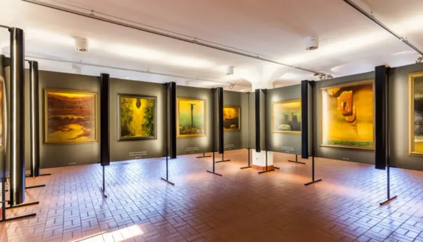 Wystawa obrazów Beksińskiego w galerii, z widocznymi dziełami w żółtych i brązowych barwach.