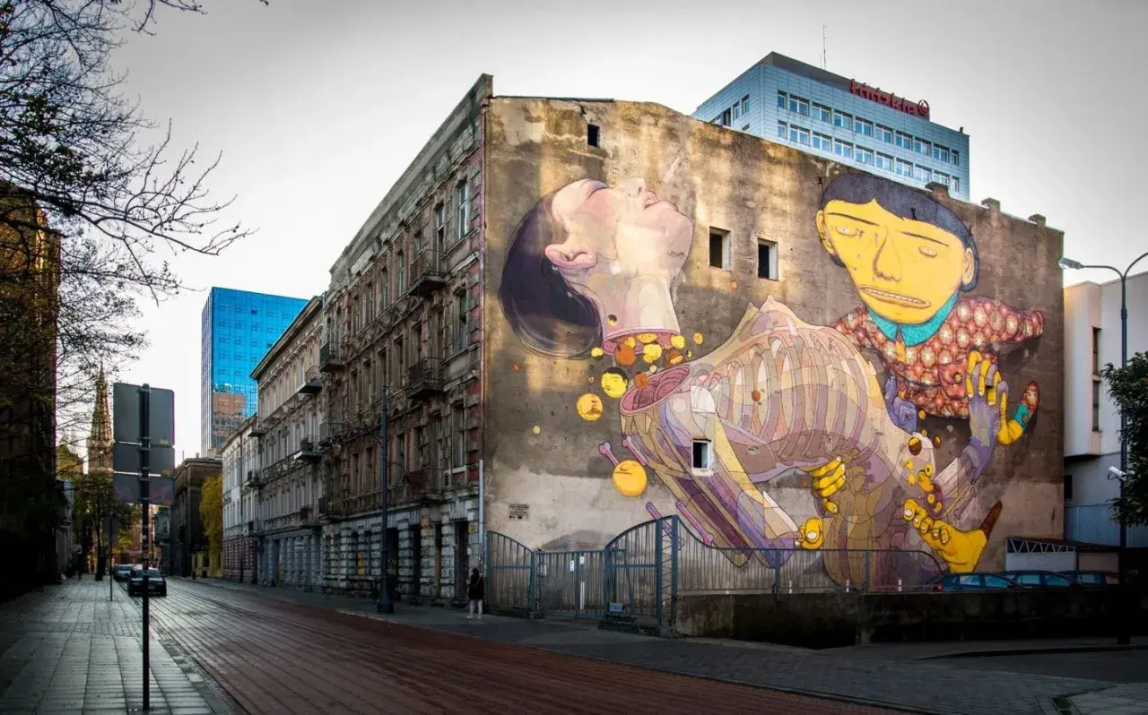 Kolorowy mural na ścianie kamienicy przedstawia surrealistyczną scenę z postaciami i elementami anatomicznymi.