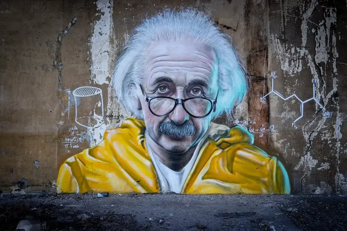 Portret Einsteina, ubranego w żółtą bluzę, z wzorami chemicznymi i równaniami na ścianie. Prawdziwy człowiek renesansu.